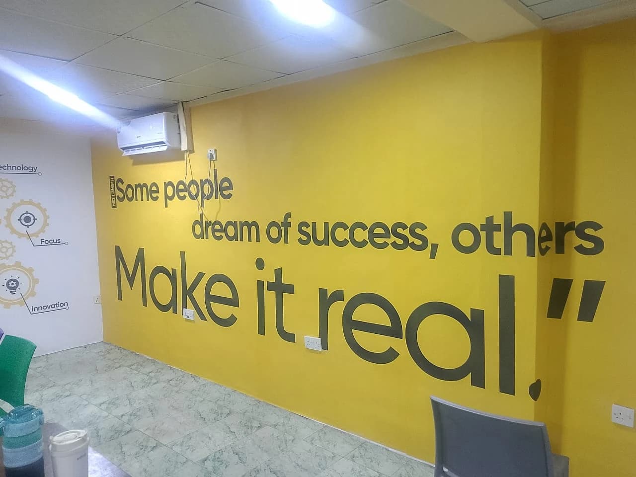 Dark charcoal motivational quote cut in matte vinyl installed across a bright yellow office accent wall.