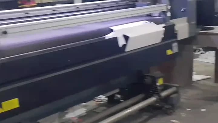 Industrial wide-format roll-to-roll printer outputting heavy PVC banner roll in an active print shop.