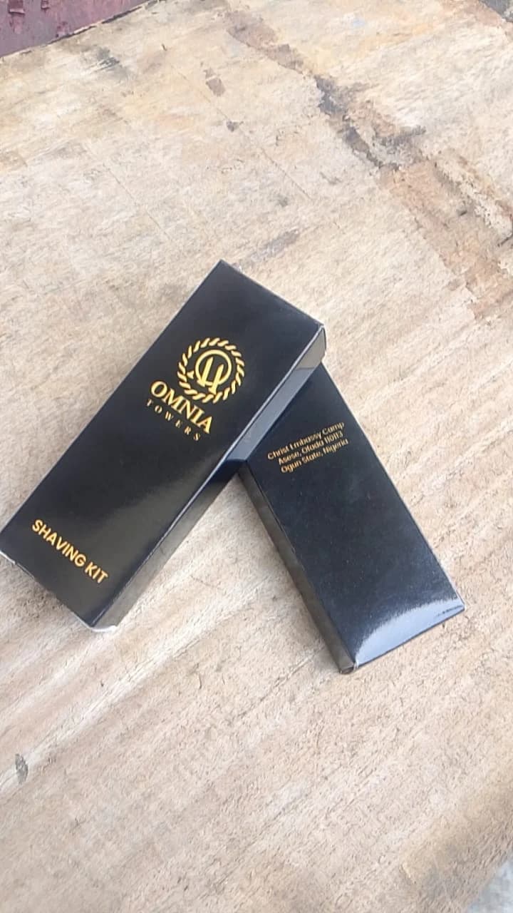 Two black gloss shaving kit packaging boxes with metallic gold foil stamped Omnia Towers logos.