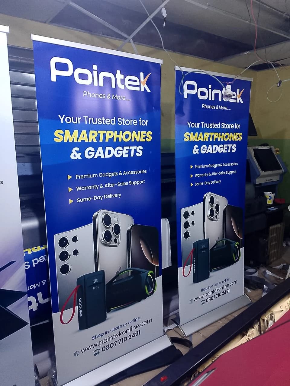Two tall blue Pointek retractable roll-up banner stands displayed next to a wide-format printer.