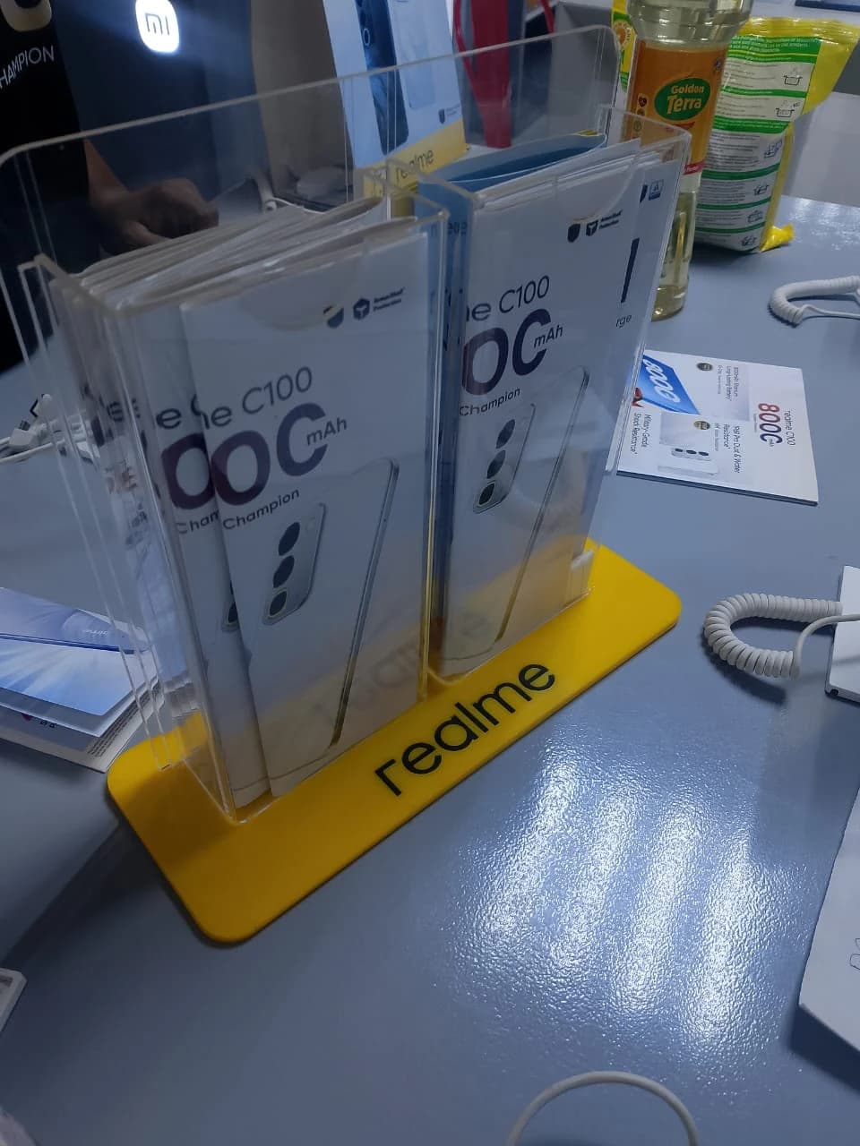 Yellow branded realme acrylic counter display stand holding printed C100 smartphone promotional leaflets.