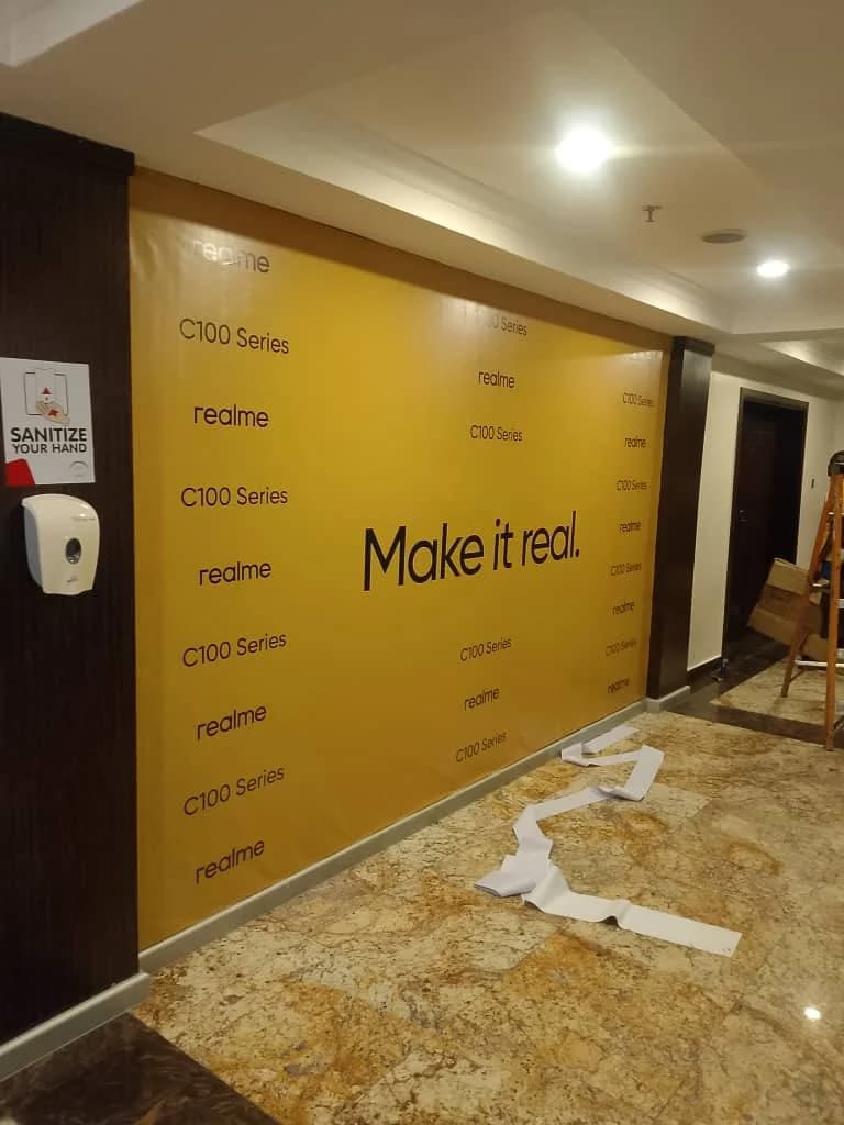 Bright yellow realme C100 Series branded event backdrop media wall installed in a Lagos hotel venue hall.