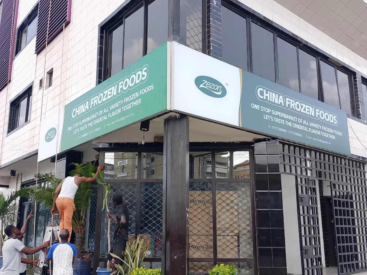 Installation crew mounting green and white wrap-around composite fascia signage for China Frozen Foods in Lagos.