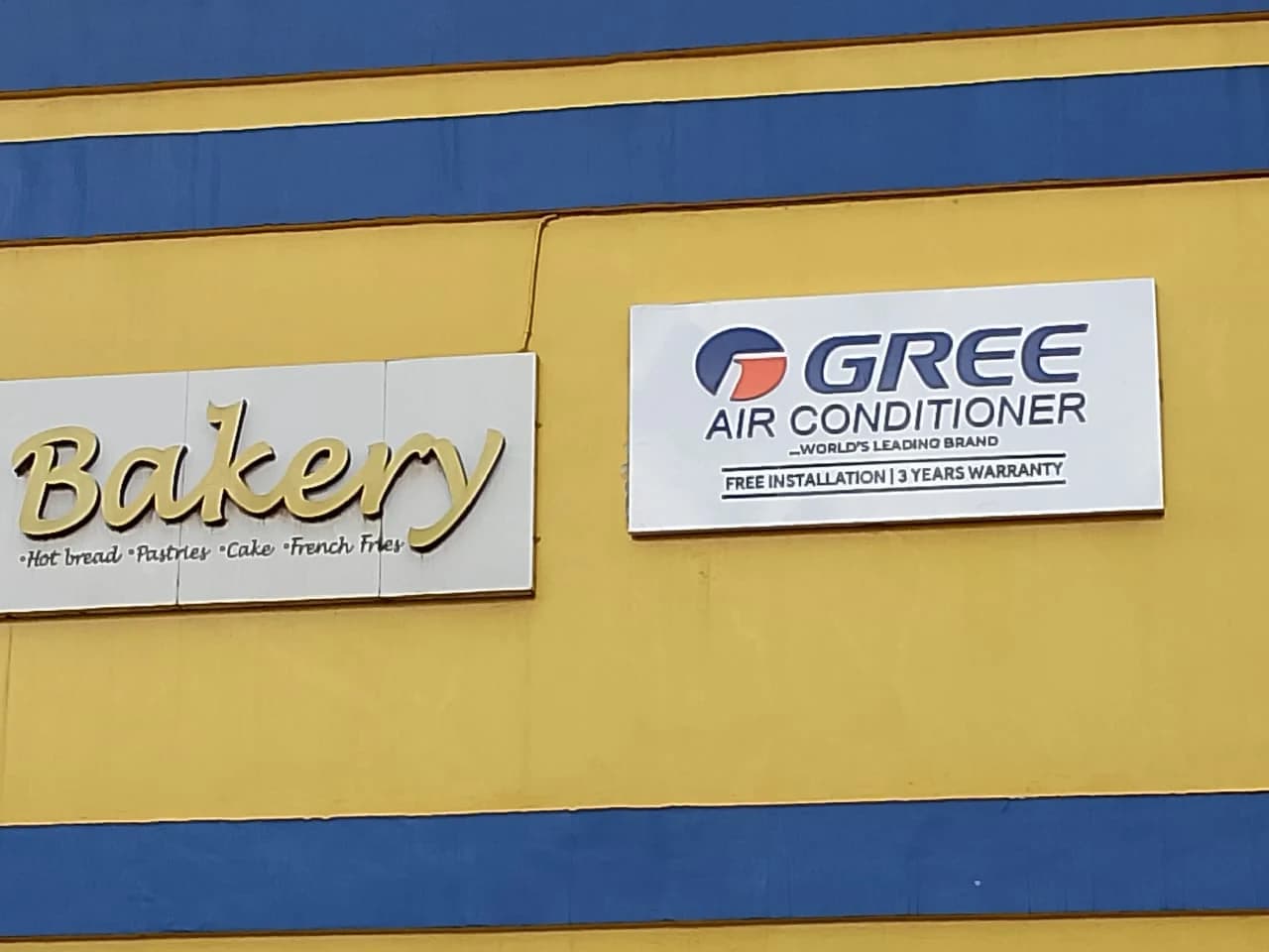 White GREE Air Conditioner aluminium composite fascia sign tray installed on a yellow commercial building facade.